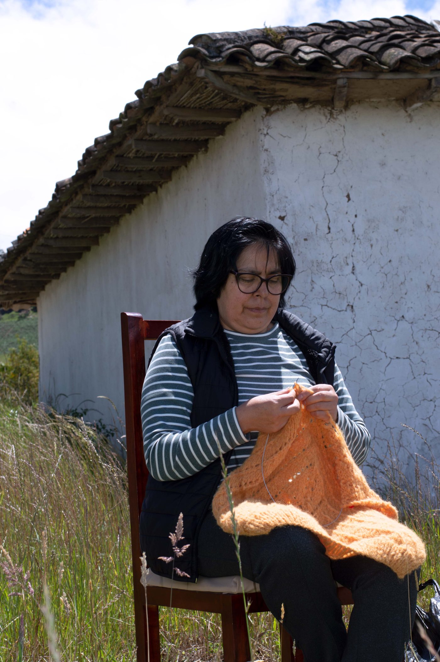 A tejedora knitting with orange yarn in Carchi